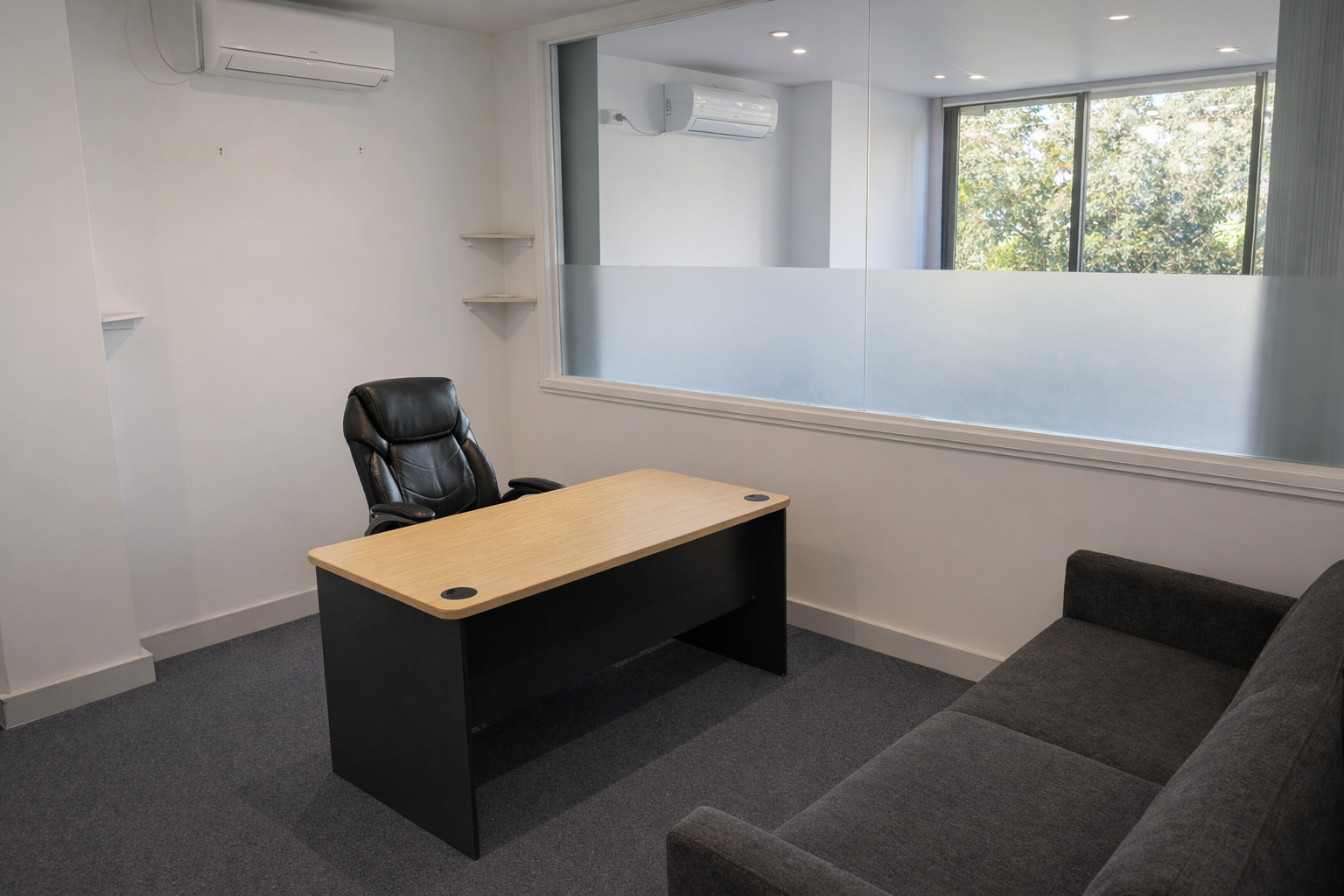 Private office with wooden desk, executive chair, sofa, and natural light through large windows